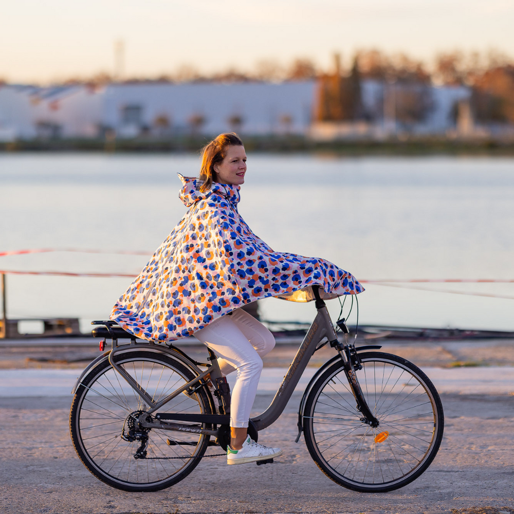 Utilisateur à vélo portant la cape Cap Canaveral 100 % recyclée, protection imperméable et visibilité renforcée.