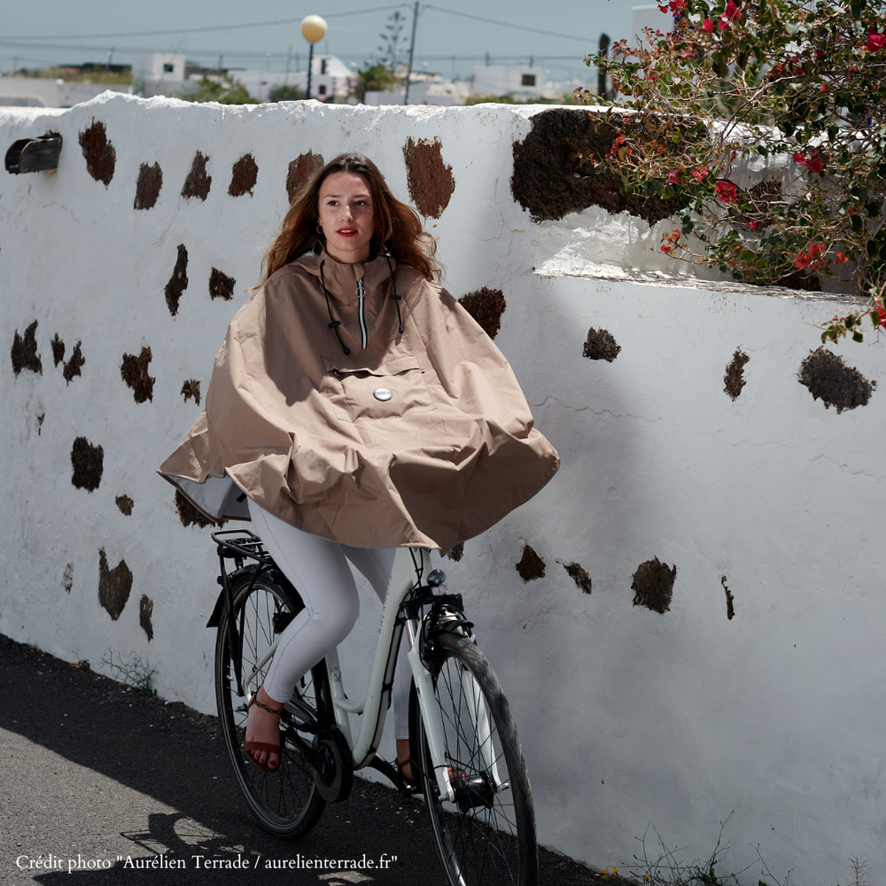 Personne à vélo sous la pluie portant la cape Cap Cod beige recyclée, protection imperméable.