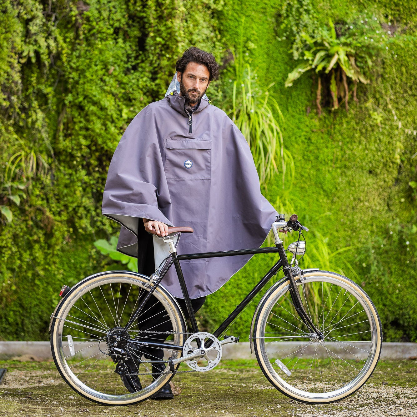 Utilisateur à vélo sous la pluie portant la cape Cap Nordkinn Grise, protection imperméable pour trajet urbain.