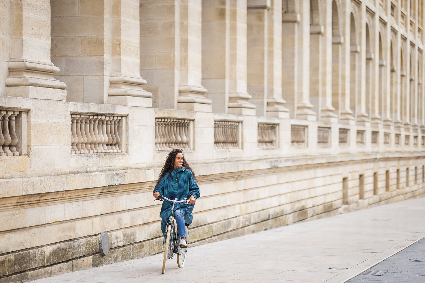 Utilisateur à vélo portant le poncho Anvers en pied de poule vert et bleu marine, coupe ample avec capuche, protection imperméable contre la pluie.