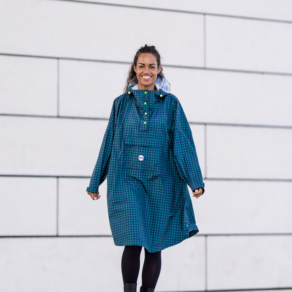 
                      
                        Poncho Anvers en pied de poule vert et bleu marine avec pochette de rangement intégrée et finition boutons jaune.
                      
                    