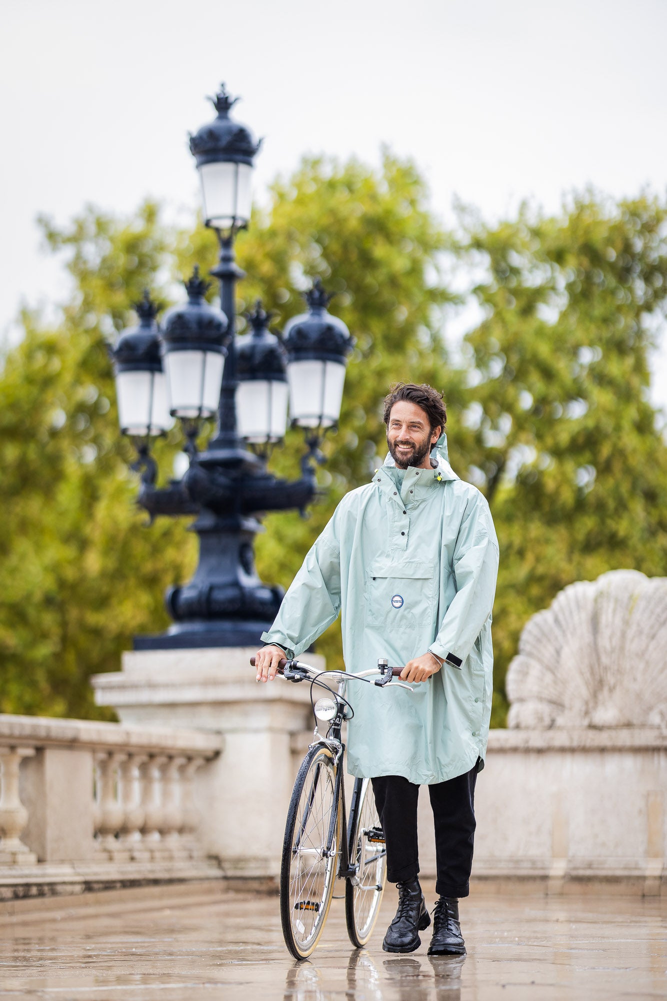 Personne à vélo portant le poncho Genève bleu glacier, sous la pluie, coupe ample avec capuche, protection imperméable.