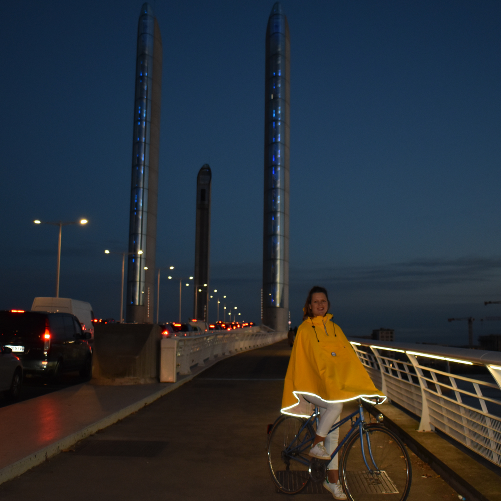 
                      
                        Utilisateur à vélo la nuit portant la cape Cap Breton recyclée, avec bandes réfléchissantes visibles pour une sécurité renforcée.
                      
                    